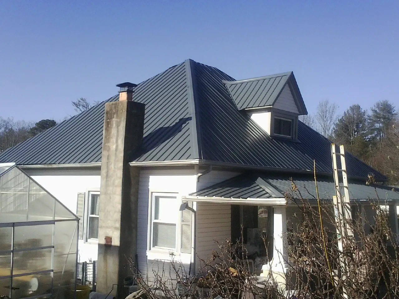 Dark blue standing seam metal roof on a white farmhouse with dormer — Slate & Tile Roof Repair by Roofing Brothers in Clio