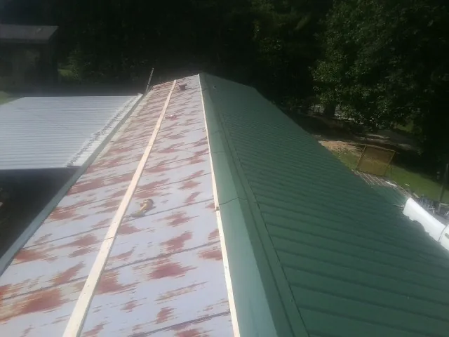 Old rusted panels beside newly installed green metal roofing — Wind Damage Roof Repair by Roofing Brothers in Clio