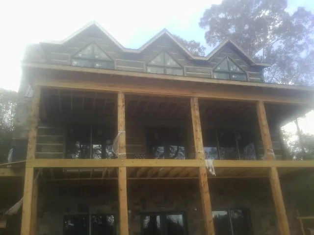 Dormers and porch framing on a large log home under construction — Roof Coating work by our crew in Clio