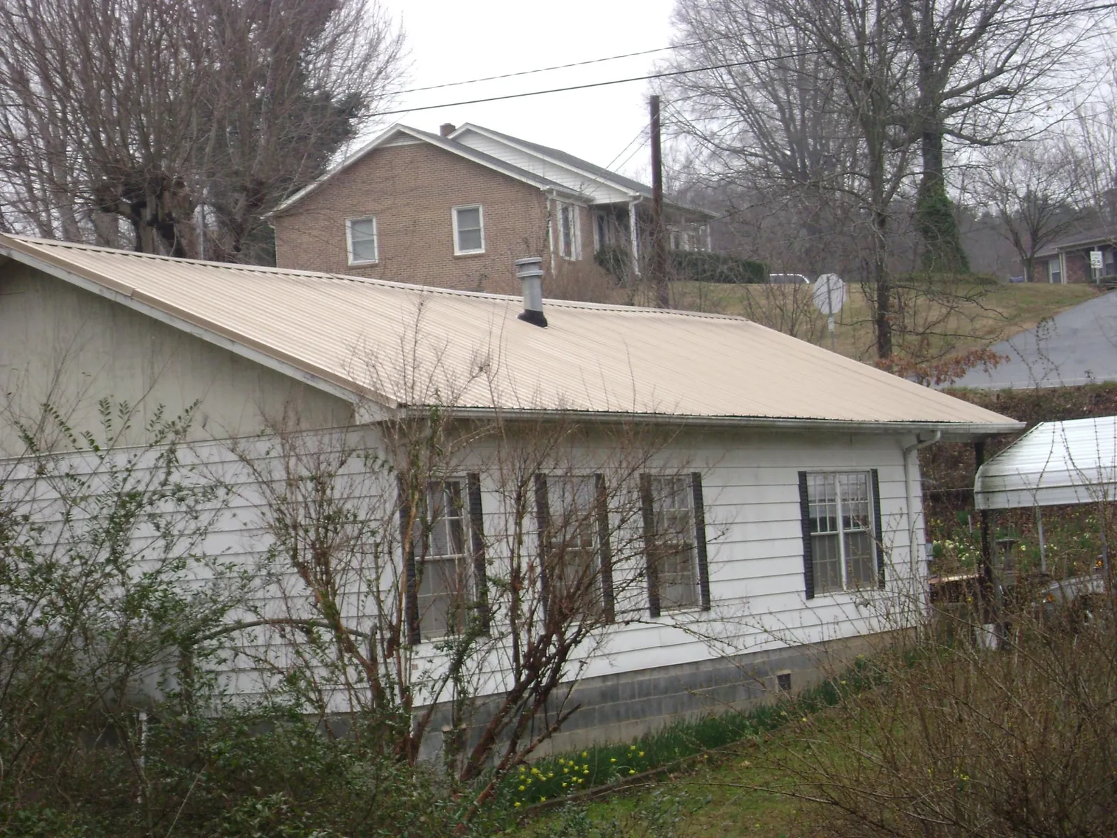 Tan metal roof on a white sided house set into a hillside — Commercial Roofing by Roofing Brothers in Clio